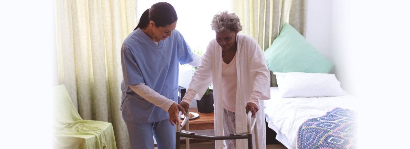 Front view of mixed race female nurse helping senior mixed race female patient to stand with walker at nursing home