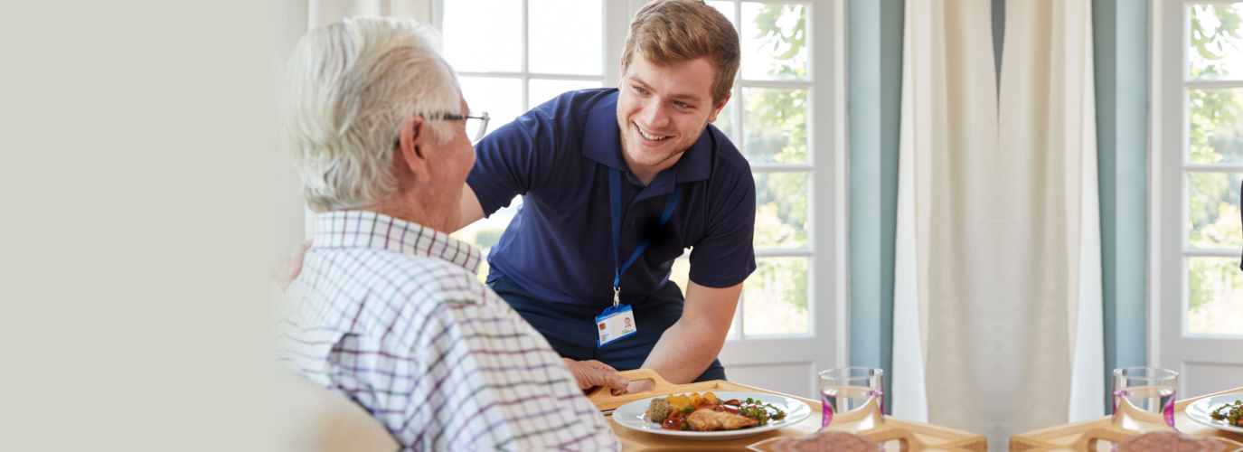 Male care worker serving dinner to a senior man at his home